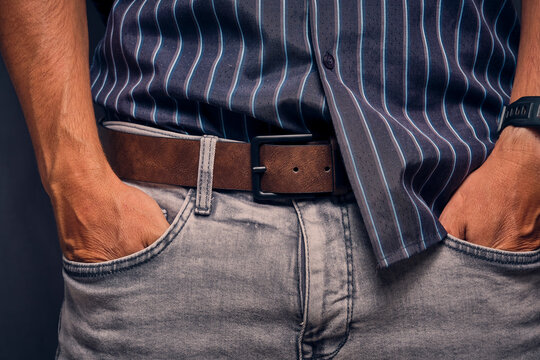 Man wearing striped shirt and grey jeans standing with both hands inside front pockets close up.