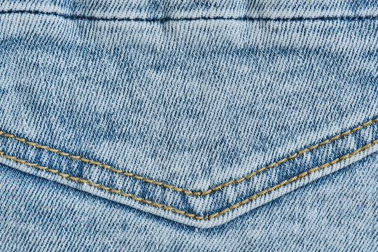 Macro texture light blue denim fabric with double yellow stitched seam on back pocket detail.