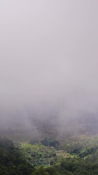 Vertical video. Dramatic View of Gunung Batur Volcano Partly Hidden by Low Clouds Above Lush Tropical Valley. Adventure Travel, Natural Wonder, Volcanic Landscape
