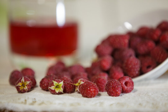 Fresh ripe red raspberries spilled on a table with a blurred glass of juice.