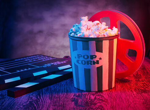 Cinema movies concept background, with a pop corn bucket, 3D glasses, a clapperboard and a tape spool. Movie night template, table top photography commercial shot, with a retro purple, aesthetic.