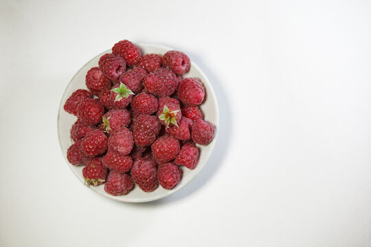Fresh ripe red raspberries in a white ceramic bowl on a white background with copy space.