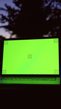 Vertical video. Open Laptop With Green Screen Mockup Standing Near Illuminated Swimming Pool at Tropical Resort During Twilight, Remote Work, Digital Nomad Lifestyle, Travel Technology