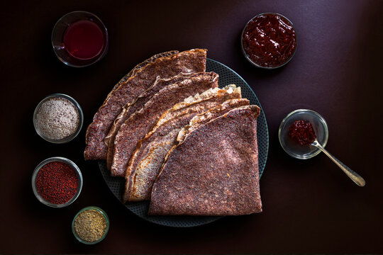 Close-up of ragi-based crepes (made from finger millet), with small bowls containing whole ragi and ragi ground into flour, along with a few ingredients served alongside the crepes