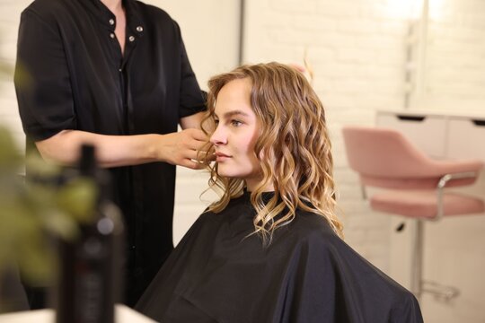 Hairdresser styling woman's hair in beauty salon, closeup