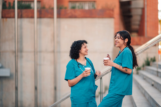 Healthcare workers enjoying coffee break, smiling and having a conversation on hospital stairs
