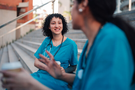 Healthcare professionals sitting outside on hospital stairs, enjoying a coffee break, talking and relaxing together