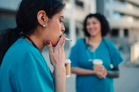 Healthcare worker smoking during coffee break, finding stress relief in unhealthy habit outside hospital building