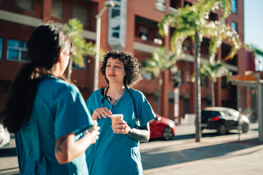 Healthcare professionals in scrubs enjoying coffee break on a city street, conversing and relaxing outdoors