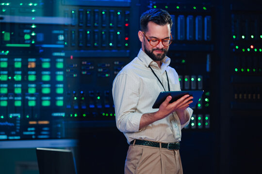 It engineer monitoring data center servers, checking network infrastructure performance with a tablet computer