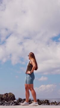 Vertical video. Wide Angle View of Woman Standing Near Rocky Coastline Watching Massive Ocean Wave Crash Against Cliffs in Slow Motion, Freedom And Adventure Travel