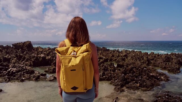 Back View of Woman With Backpack Standing Above Rocky Tide Pools Near Ocean Coastline, Adventure And Outdoor Travel