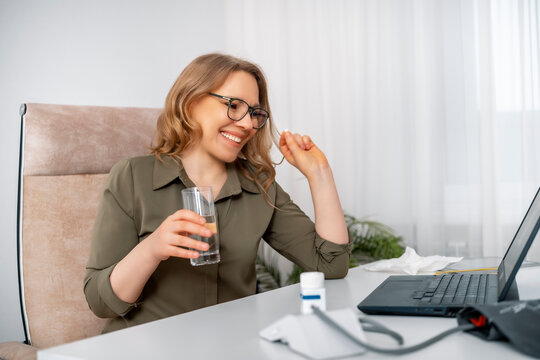 Happy woman taking pill with glass of water at office desk for relief. Health recovery, pain relief concept, wellness solution.