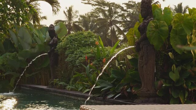 Elegant Stone Statues Spraying Water Into Tropical Resort Pool Surrounded by Lush Exotic Plants at Golden Sunset