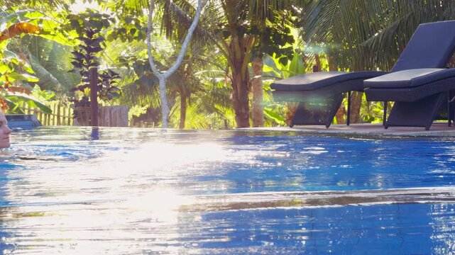 Young Woman Floating In Resort Pool With Tropical Palm Trees And Sun Loungers In Background, Relaxation And Wellness
