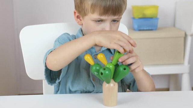 Boy works with colorful wooden cactus tree puzzle at home table in bright room in wide scene. Montessori home education and independent learning space concept.