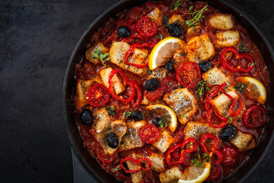 Slow cooked fish stew with tomato souce, vegetable and olives served as top view in a cast iron casserole
