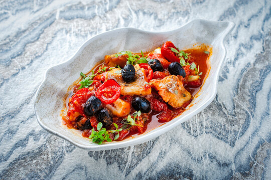 Slow cooked fish stew with rice, tomato souce, vegetable and olives served as close-up in a shell design bowl