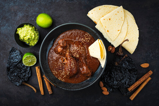 Traditional authentic artisan spicy chicken mole poblano in a bowl with avocado guacamole and fresh tortilla served as top view