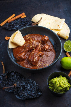 Traditional authentic artisan spicy chicken mole poblano in a bowl with avocado guacamole and fresh tortilla served as close-up in a design bowl