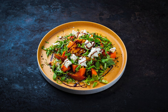 Fresh made spring mixed salad with arugula, sweet potato, feta sheep milk cheese and caramelized nectarines with balsamico cream served as close-up on a design plate
