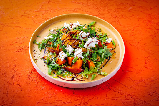 Fresh made spring mixed salad with arugula, sweet potato, feta sheep milk cheese and caramelized nectarines with balsamico cream served as close-up on a design plate