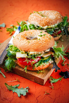 Classic fingerfood fastfood snack -  traditional sesam bagels - bread rolls sandwich with avocado guacamole, cheese and vegetable salad served as close-up on a wooden board