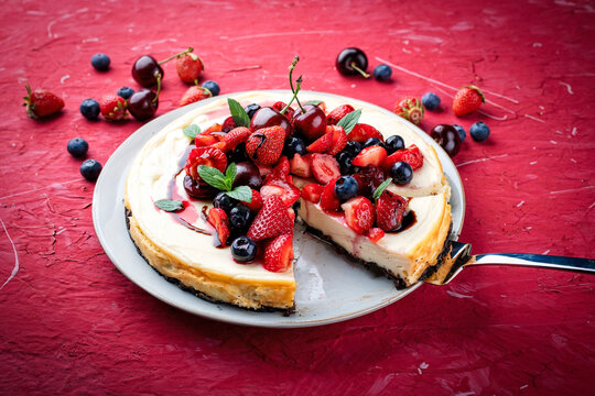 Artisan homemade New York cheesecake pie with fresh strawberries, blueberries and cherries and balsamic cream sauce served as close-up on a design cake plate