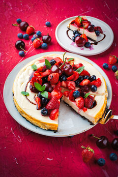 Artisan homemade New York cheesecake pie with fresh strawberries, blueberries and cherries as topping and balsamic cream sauce served as close-up on a design plate