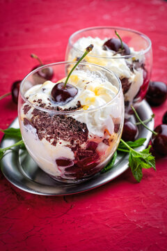 Parfait dessert with whipped cream,  mascarpone fresh cream cheese, dark chocolate and sour and sweet cherries served as close-up in a glass