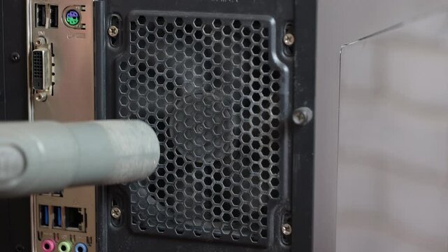 Person cleaning a dusty computer power supply with a vacuum cleaner. Thorough computer maintenance process involving a vacuum cleaner removing dust and dirt from the power supply unit fan