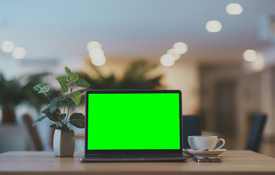 Mockup of laptop computer with empty screen with coffee cup and smartphone on table of the coffee shop background,Green screen