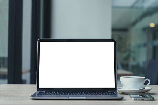 Mockup of laptop computer with empty screen with coffee cup and smartphone on table of the coffee shop background,White screen