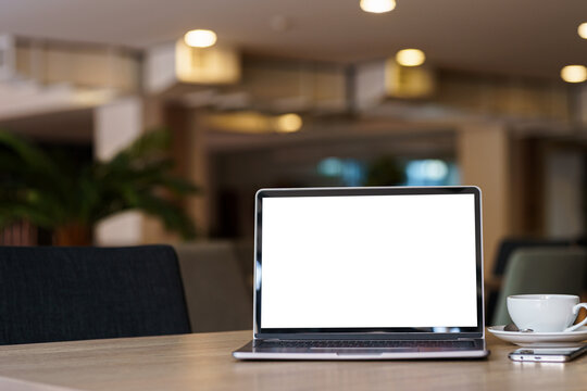 Mockup of laptop computer with empty screen with coffee cup and smartphone on table of the coffee shop background,White screen