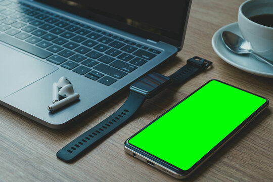 Close-up of Keyboard laptop computer, wireless earphones, smartwatch and smartphone empty screen on wooden background office desk in coffee shop like the background,Green screen