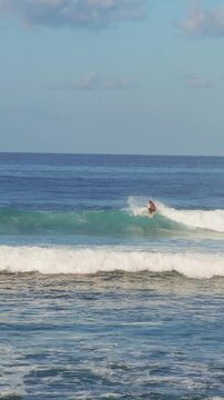 Vertical video. Surfer Gliding Across Blue Ocean Wave During Sunny Day, Adventure Travel And Water Sports