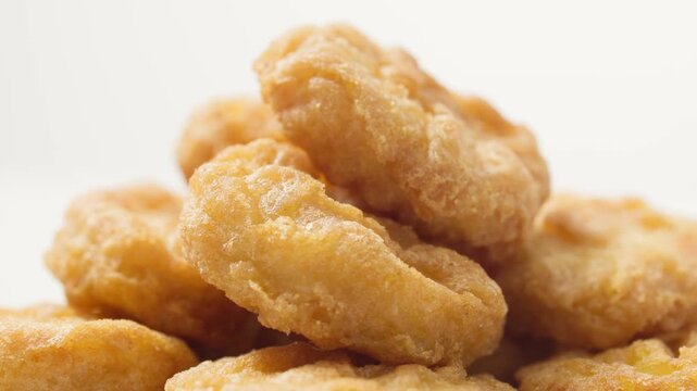 Close-up of a stack of crispy chicken nuggets slowly rotating on a white background. Golden fried bite-sized chicken pieces with a crunchy coating, for clean commercial use. Premium food video