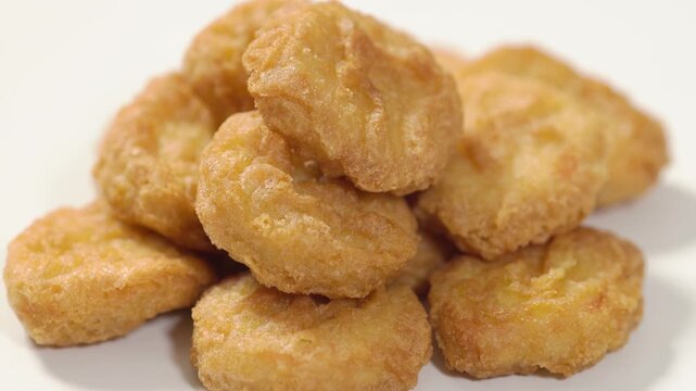 Close-up of a stack of crispy chicken nuggets slowly rotating on a white background. Golden fried bite-sized chicken pieces with a crunchy coating, for clean commercial use. Premium food video