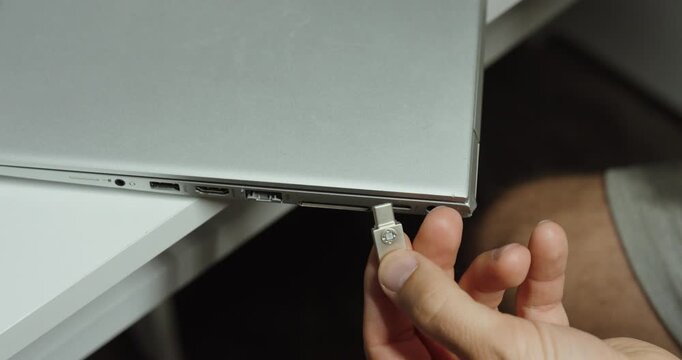 Close-up of a man plugging a USB-C flash drive into a laptop for data transfer, storage, and computer connectivity.