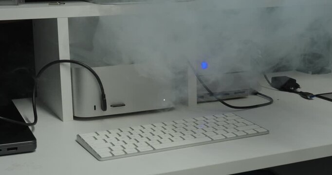 A desktop computer begins releasing smoke, illustrating an electrical malfunction, overheating, or potential fire hazard in a workstation.