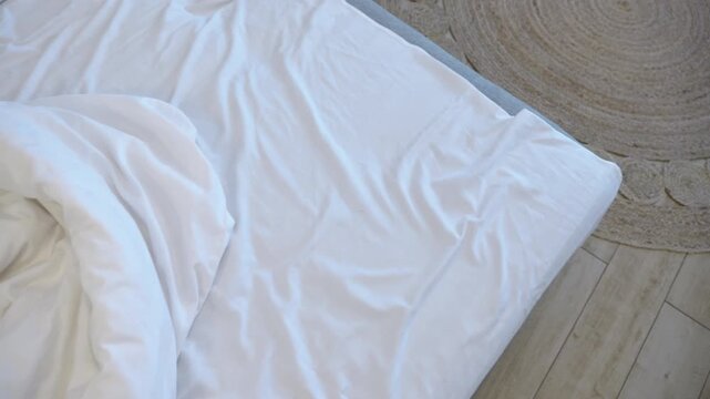 Unmade bed revealing pillows and duvet. Empty unmade bed with crumpled white linen, duvet, and pillows in a bright, modern bedroom with wooden floors. Morning routine concept of making the bed