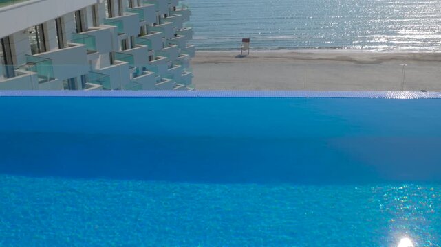 Luxury hotel infinity pool overlooking ocean beach. Stunning view from a rooftop infinity pool at a luxury hotel, overlooking a sandy beach and the calm, shimmering sea on a beautiful sunny day
