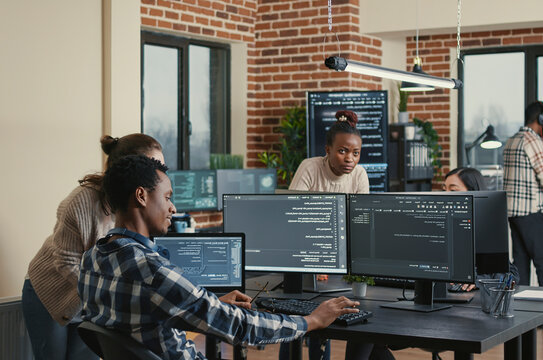 Programmer analyzing compiling code on multiple screens takes off glasses and doing high five hand gesture with colleague developer, software developers celebrating successful coding.