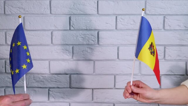 European union and moldova flags coming together. Male and female hands bringing the flags of the european union and moldova together, symbolizing international cooperation, diplomatic relations