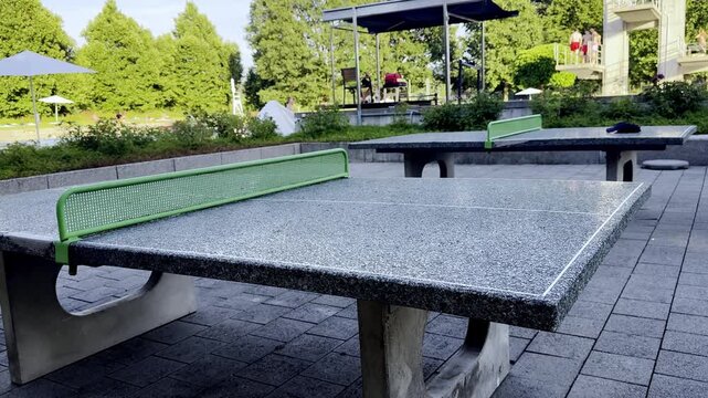 Outdoor Stone Table Tennis Table with Green Net in a Public Park, Second Ping Pong Table and People Walking in the Background, Sunny Summer Day, Recreational Area, Switzerland