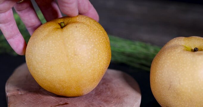 Half a pear and slices, crushed pear fruit are on the surface of a wooden circle against a dark matte stone background in the frame.