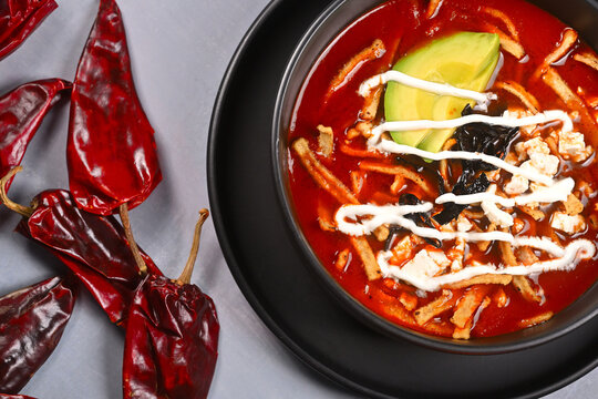 Top view of authentic Mexican tortilla soup topped with avocado slices, sour cream, and pasilla chili
