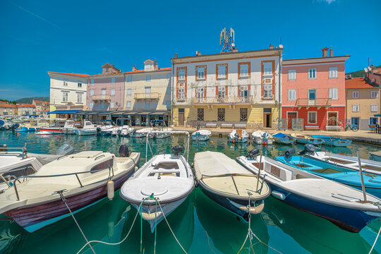 Cres town displaying its historic Venetian architecture and vibrant buildings along the harbor, with numerous boats moored in emerald green Kvarner Gulf under summer sky of Cres Island in Croatia.