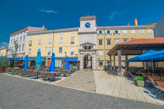Cres town square, Trg Frane Petrica, presenting classic Venetian architecture and a prominent clock tower under a clear summer sky, with outdoor cafes inviting relaxation of Cres Island in Croatia.