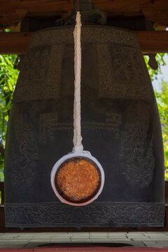Close-up of a large Korean bronze temple bell and wooden striker for buddhist rituals.